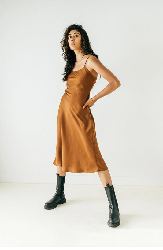 Cocoa coloured slip dress hitting mid calf, with adjustable thin shoulder and back straps that tie as bows with open lower back.