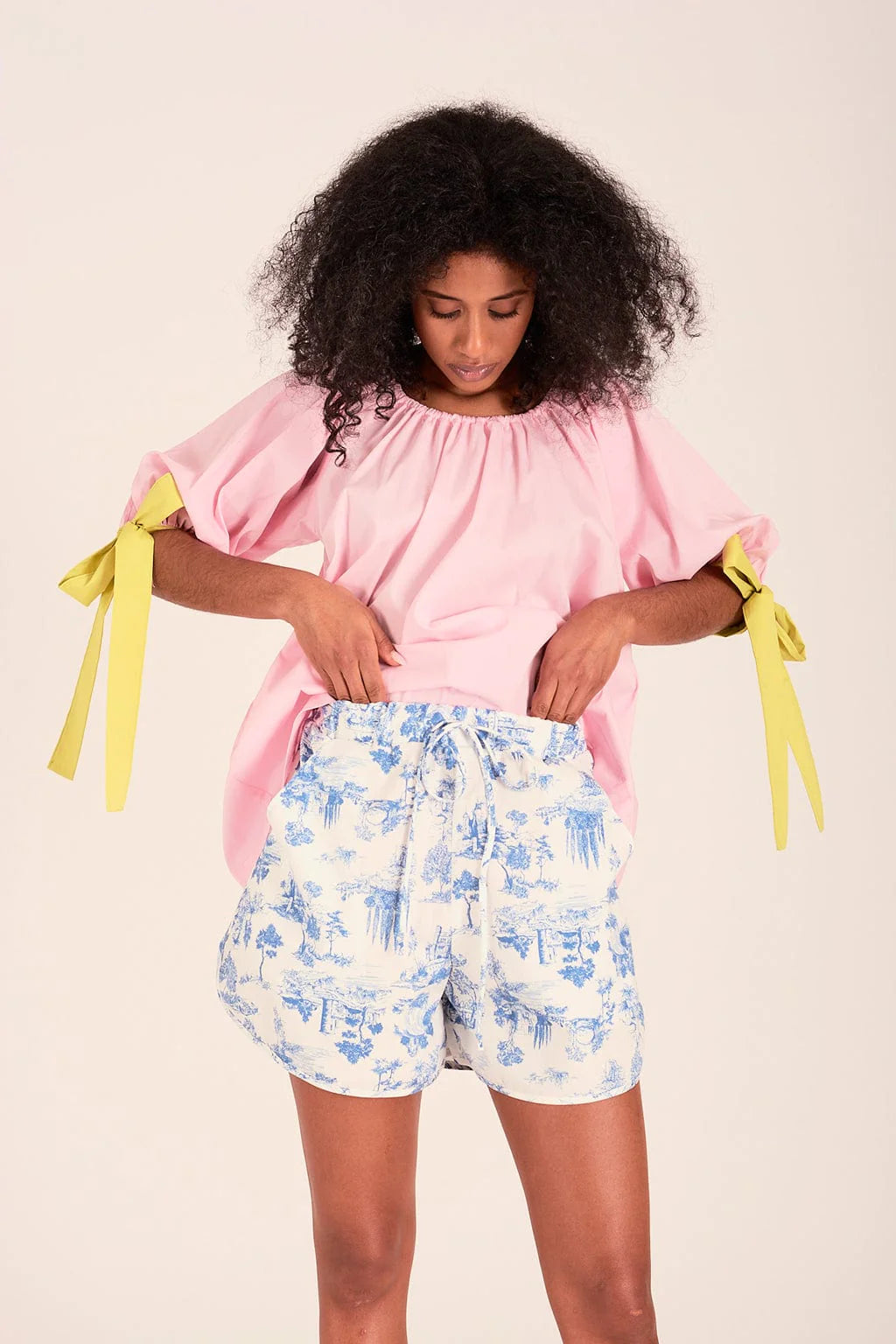 The sally top is pink with full puff sleeves that sit above the elbow with the help of big, bold adjustable green ties and an elasticized neckline so you can wear it on or off the shoulder.