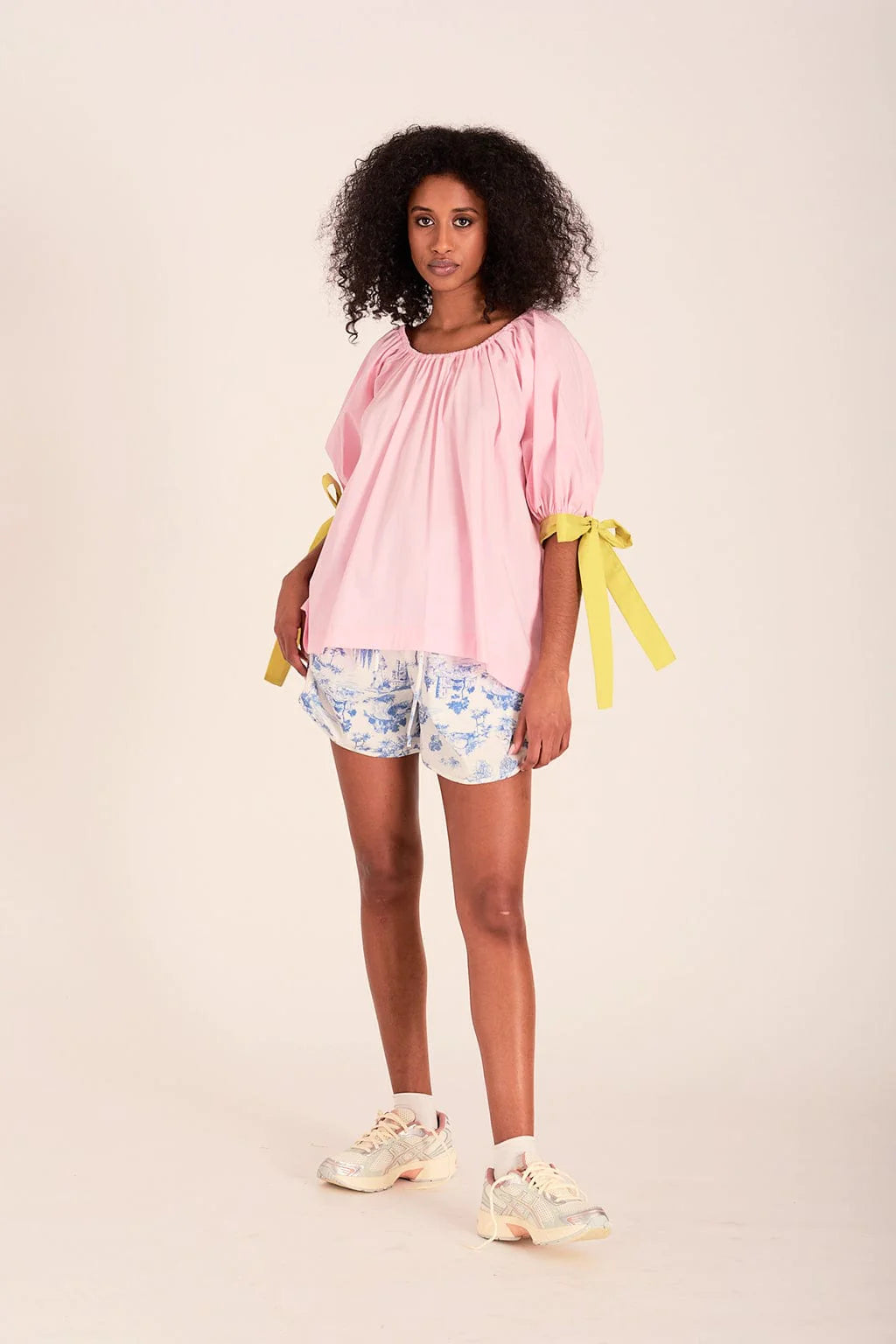 The sally top is pink with full puff sleeves that sit above the elbow with the help of big, bold adjustable green ties and an elasticized neckline so you can wear it on or off the shoulder.