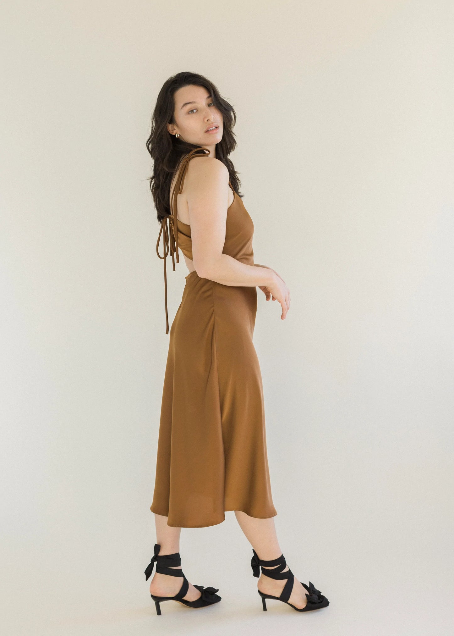 Cocoa coloured slip dress hitting mid calf, with adjustable thin shoulder and back straps that tie as bows with open lower back.