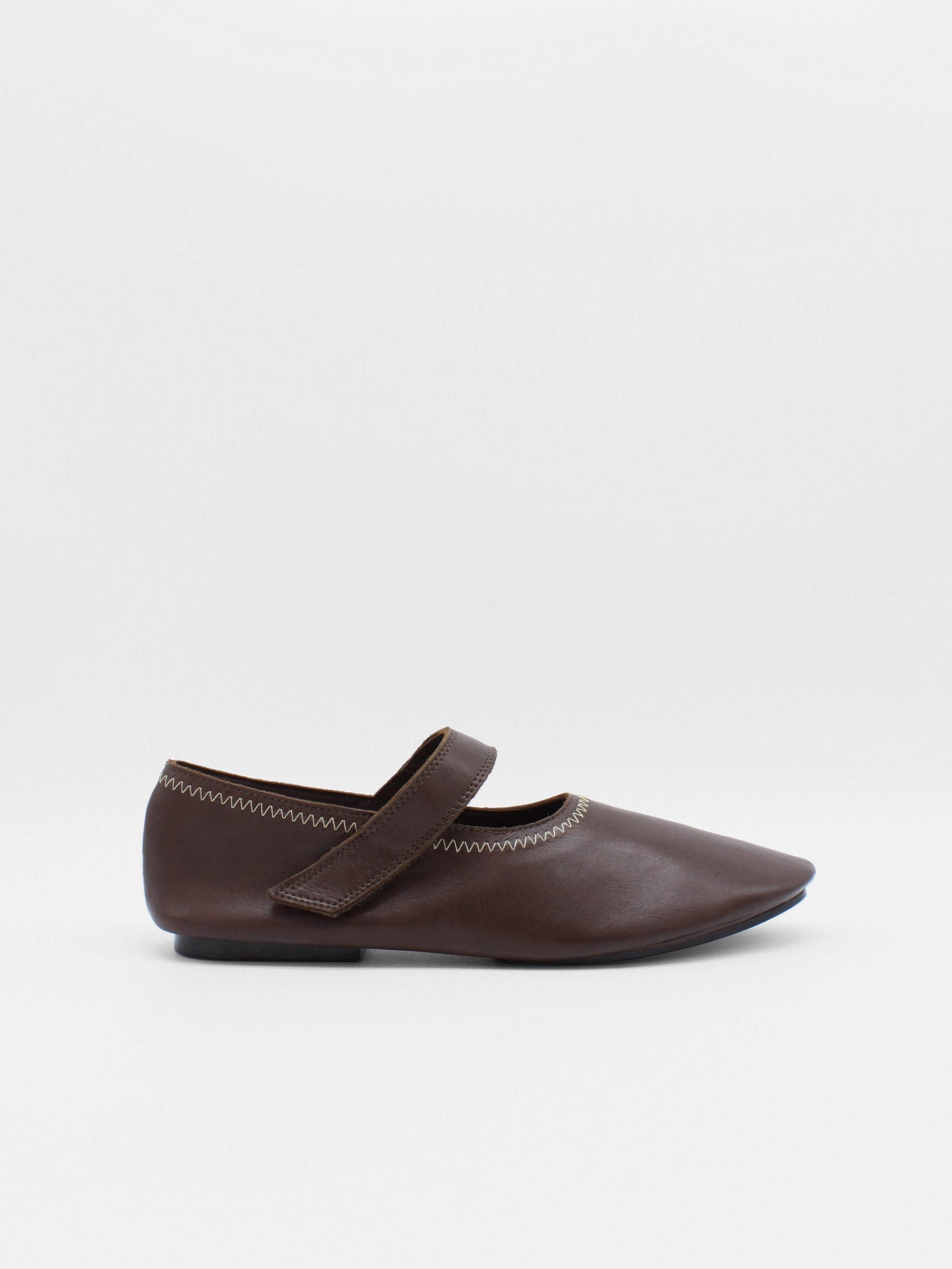 Unlined flat mary-jane made of dark brown lamb nappa leather with a shiny finish and stitching details. 