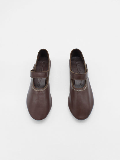 Unlined flat mary-jane made of dark brown lamb nappa leather with a shiny finish and stitching details. 