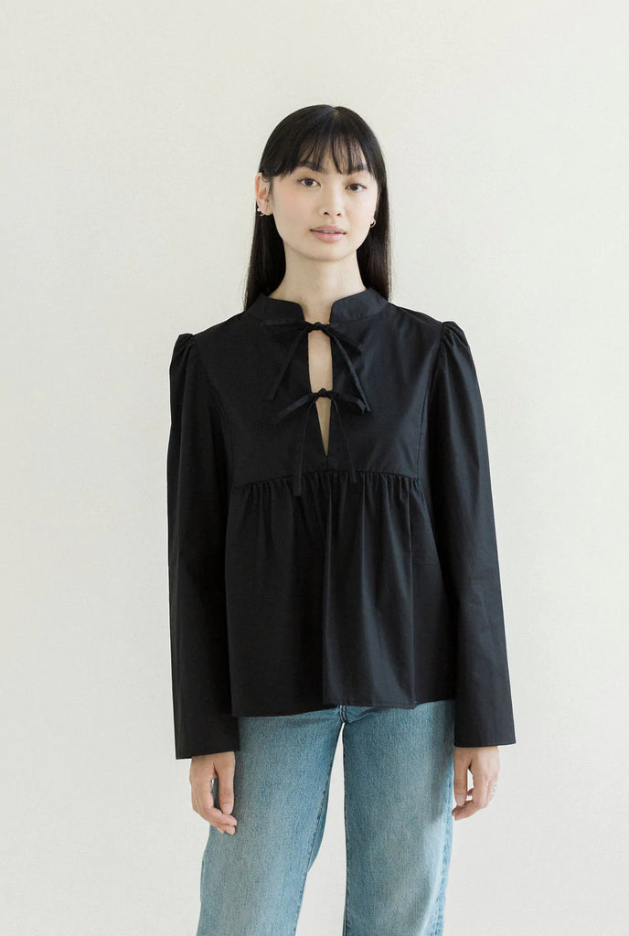 Black cotton blouse with V-neck front bib detail with 2 sets of front ties, puff shoulders, and a Manadarin collar. 