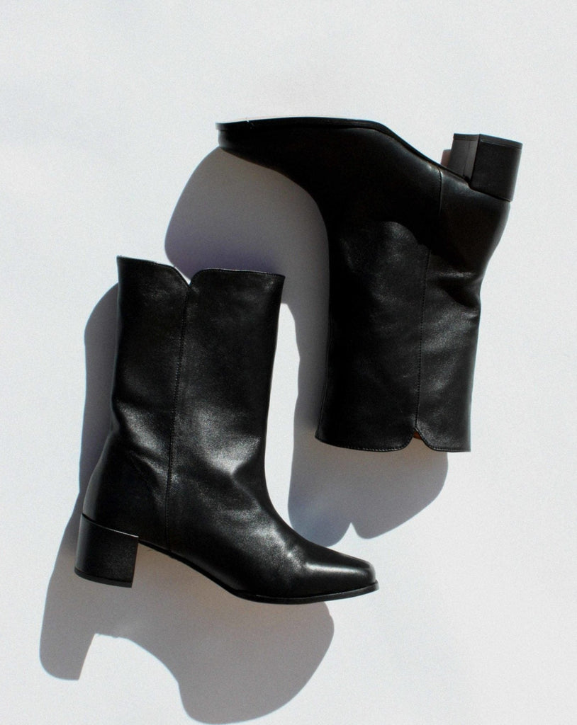 About Arianne black leather pull on boot with almond shaped toe, block heel, and v- shaped dip detail at top of shaft 