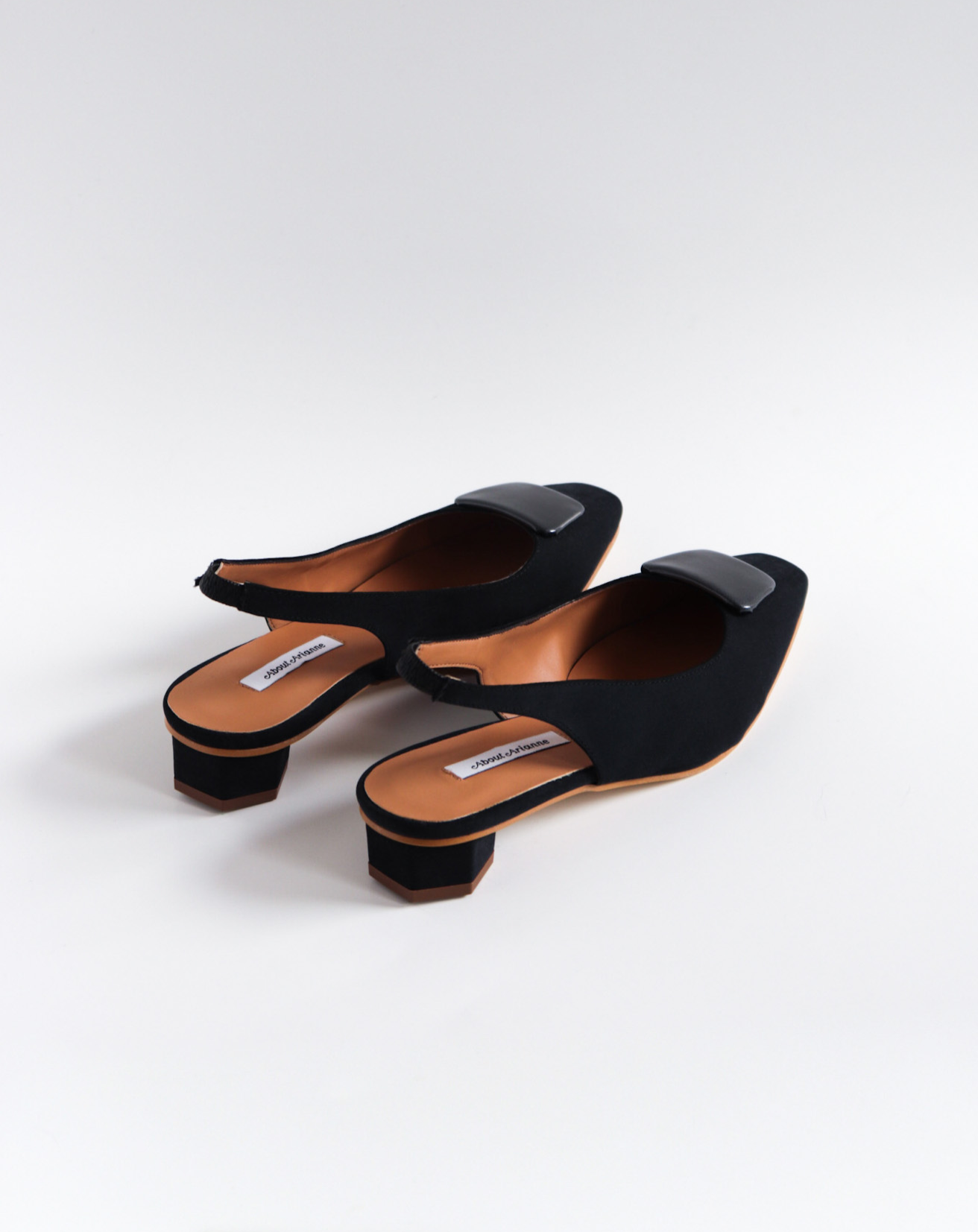 Slingback flats in a black vegan satin, made with a square toe, a unique hexagonal heel of 2.5 cm high, and an ornament piece on top that is lined with a charcoal fabric.