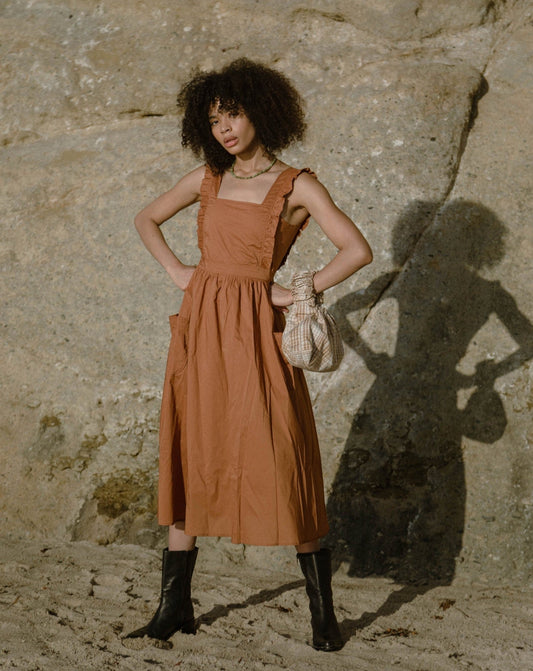Cinamon coloured apron dress with pockets, defined waist band, large straps at back to tie as bow detail, ruffled shoulder straps, and square neckline
