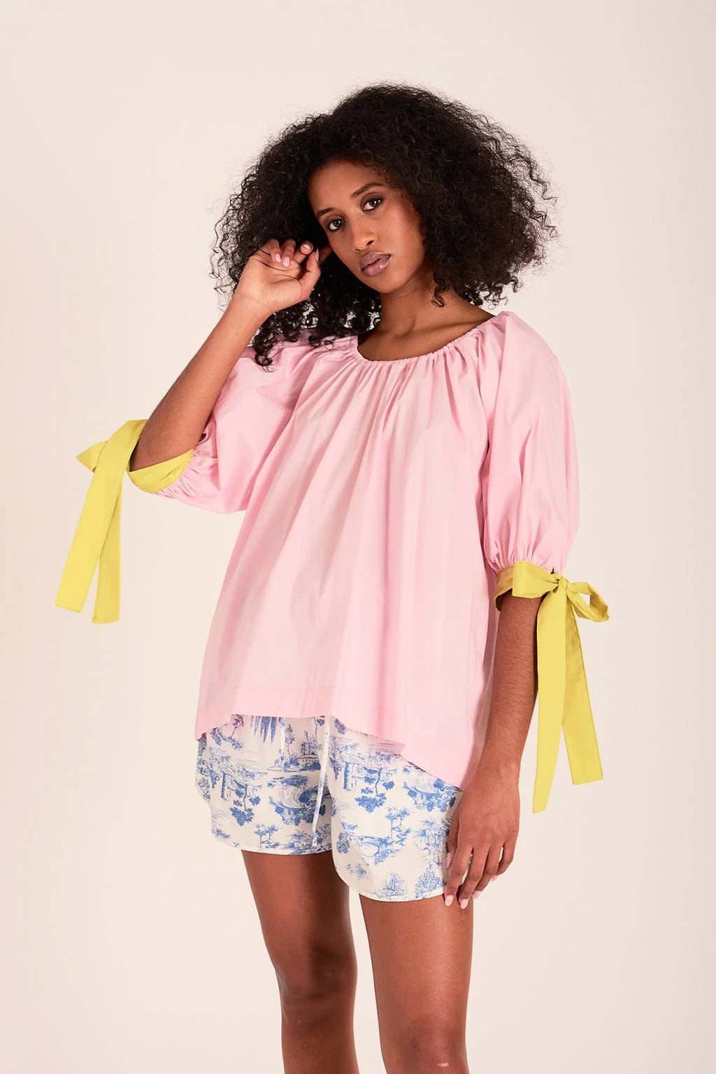 The sally top is pink with full puff sleeves that sit above the elbow with the help of big, bold adjustable green ties and an elasticized neckline so you can wear it on or off the shoulder. 