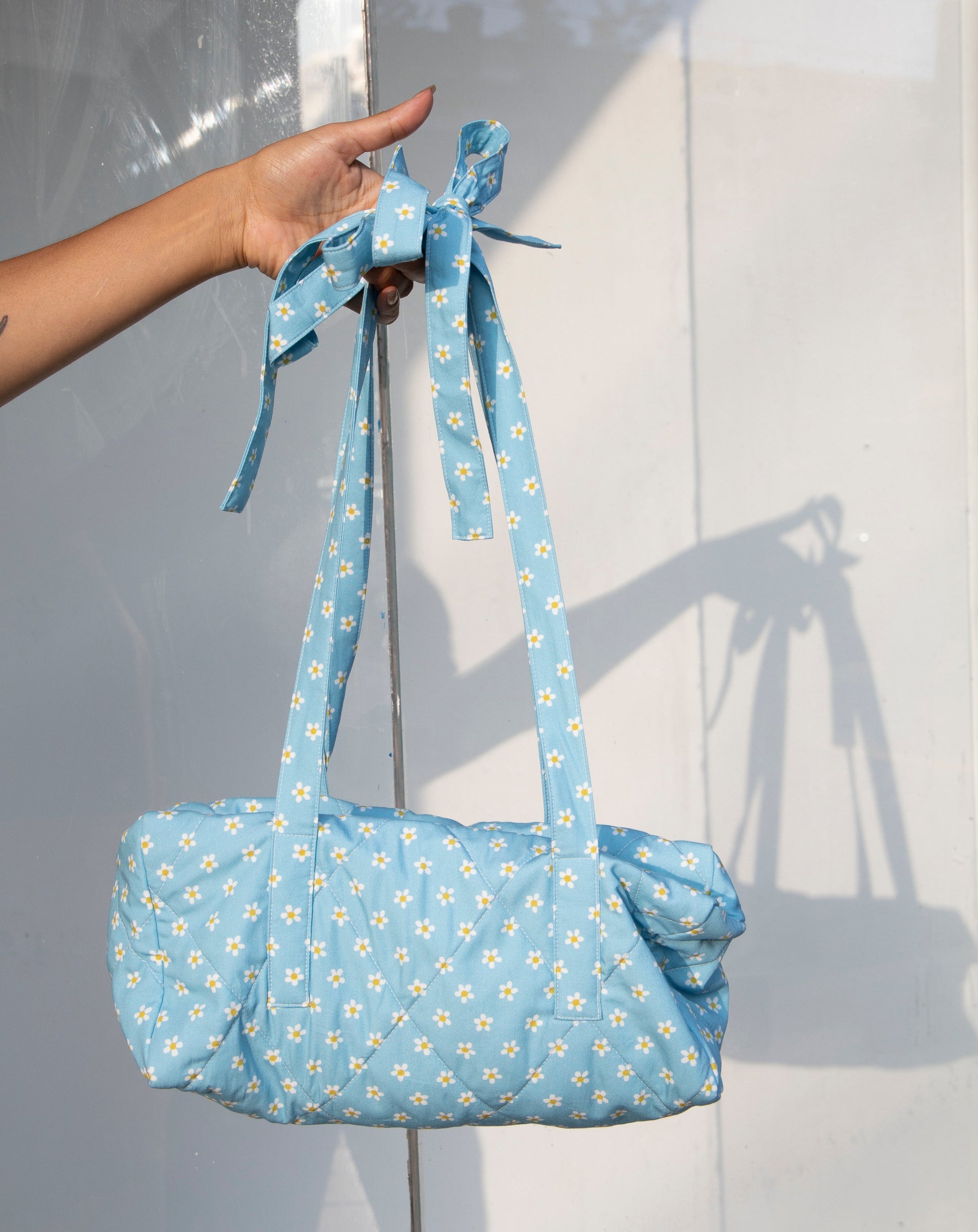 Blue daisy quilted duffle bag with shoulder straps that tie into bows. Zipper closure.  Available at Ease Toronto