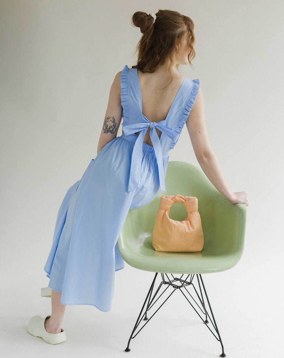 Light blue coloured apron dress with pockets, defined waist band, large straps at back to tie as bow detail, ruffled shoulder straps, and square neckline